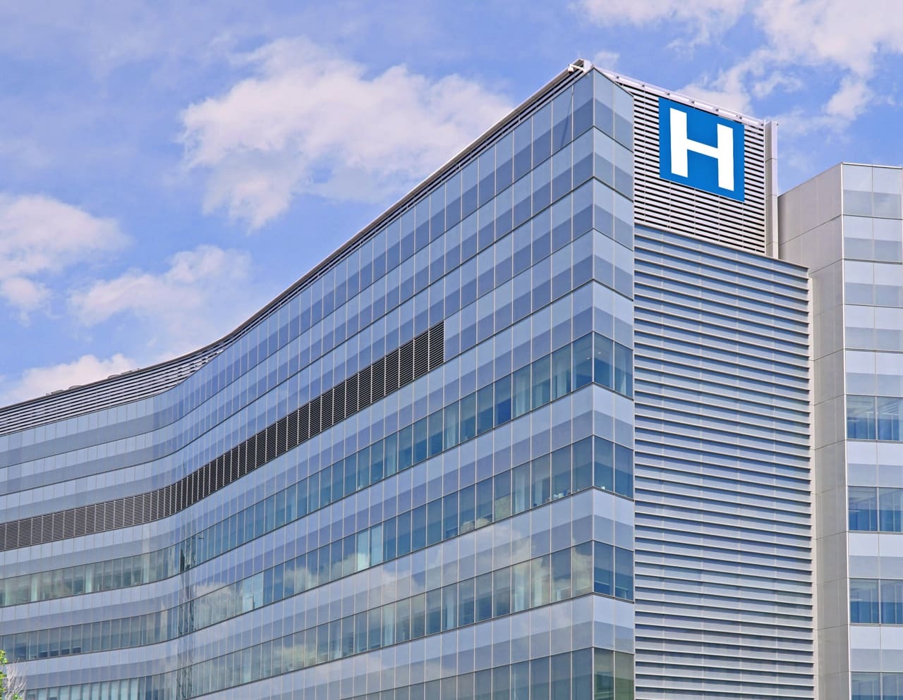 Façade vitrée d’un hôpital moderne, signalée par un grand H bleu